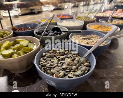 Keramikschüsseln, die auf einer Marmorarbeitsplatte angeordnet sind, servieren verschiedene frische Zutaten für eine Salatbar und fördern nahrhafte Essensoptionen und gesunde Lebensmittelauswahl Stockfoto