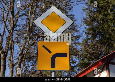 Standard-Trafikschilder, die Vorfahrt und Straßenkrümmung anzeigen, sind im Freien installiert und bieten klare Navigations- und Sicherheitsinformationen für Autofahrer Stockfoto