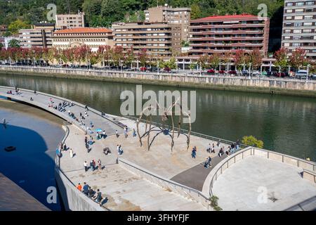 Bilbao, Spanien - 06. Oktober 2025: Blick auf die Maman-Skulptur von Louise Bourgeois auf der Promenade entlang des Nervión mit Menschen, die in der Nähe spazieren gehen. Stockfoto
