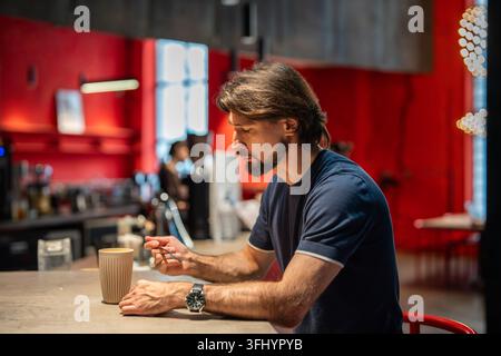Nachdenklicher Mann sitzt allein an der Theke eines Cafés mit einer Tasse Kaffee und macht eine bewusste Pause im Café. Stockfoto