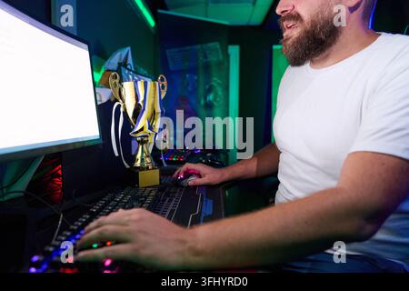 Konkurrenzfähiger Gamer feiert den Sieg mit Trophäe, während er während des Live-Streams auf RGB-PC-Setup spielt Stockfoto