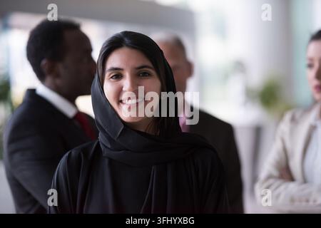 Eine selbstbewusste Geschäftsfrau mit Hijab lächelt, während sie mit multikulturellen Kollegen in einem modernen Büro steht und Professionalität, Teamarbeit vermittelt Stockfoto