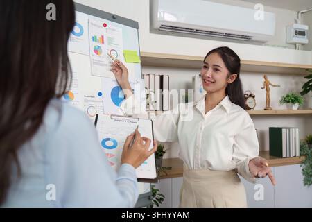 Zwei Geschäftsfrauen arbeiten zusammen an einer Finanzpräsentation, bei der sie Diagramme und Daten in einem modernen Büroumfeld diskutieren. Stockfoto