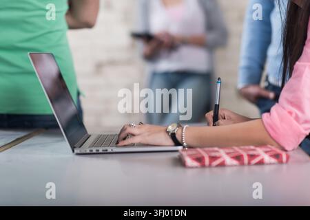 Junge nahöstliche und arabische Fachkräfte arbeiten zusammen an einem Laptop in einem kreativen Coworking-Büro eines Open-Space-Startup-Unternehmens, machen Notizen und arbeiten zusammen Stockfoto