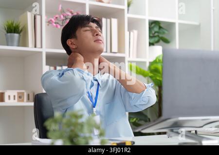 Asiatischer Mann mit Nacken- und Schulterschmerzen während der Arbeit im Büro Stockfoto
