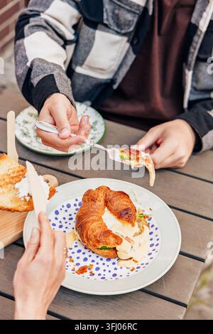 Zwei Personen teilen sich ein köstliches Croissant-Sandwich im Freien Stockfoto