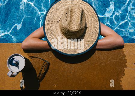 Person in einem Strohhut entspannt sich in einem Schwimmbecken Stockfoto