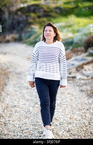 Lächelnde Frau geht entlang eines Kiesweges im Freien Stockfoto