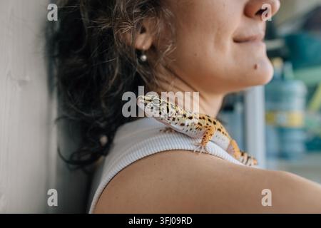 Ein niedlicher Leoparden-Gecko sitzt auf der Schulter einer Frau Stockfoto
