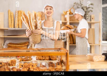 Junge Verkäuferin hält einen Korb mit frisch gebackenen Baguettes in der Bäckerei Stockfoto