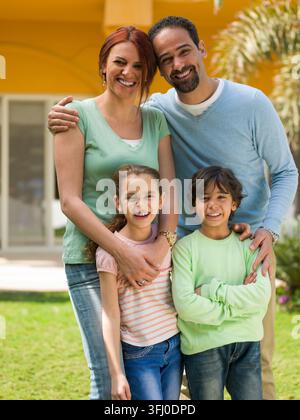 Mittelöstliche multigenerationale Familie von Eltern und zwei Kindern, die im sonnigen Garten einer modernen Luxusvilla lächeln und sich umarmen, was Wärme vermittelt Stockfoto