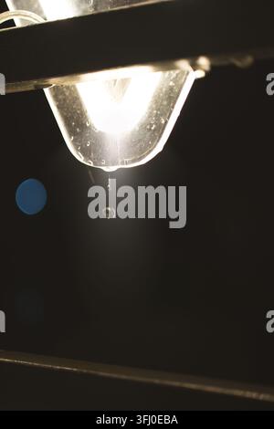 Ein Makro- und Nahaufnahmen-Foto, das einen klaren, einzelnen Wassertropfen einfängt, der sich löst und vom Rand einer nassen Glas- und Metallstruktur fällt Stockfoto