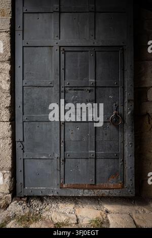 Ein detailliertes, augenhöhennahes Nahaufnahmefoto, das eine schwere, industrielle oder mittelalterliche Festungstür aus dunkelgrauem oder schwarz lackiertem Metall einfängt. Die Stockfoto