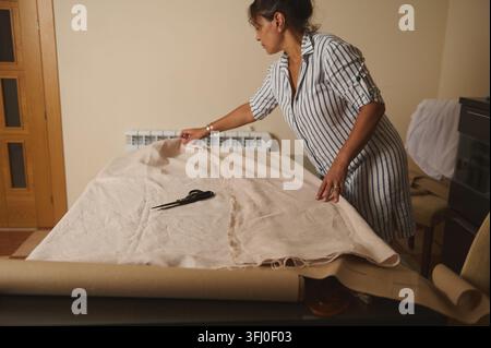 Frau bereitet Leinenstoff vor und passt ein Muster auf einem Tisch an, konzentriert auf das Schneiden und Nähen für ein Heimnäh- oder Schneiderprojekt. Stockfoto