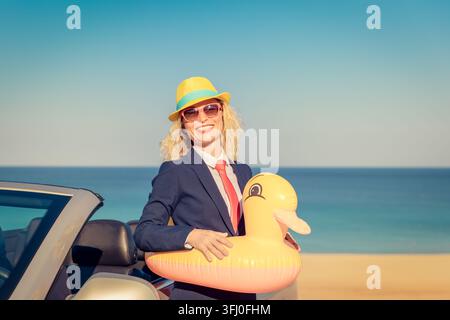 Erfolgreiche junge Geschäftsfrau am Strand. Frau, die im Oldtimer steht. Sommerurlaub und Freiheitsreisekonzept Stockfoto