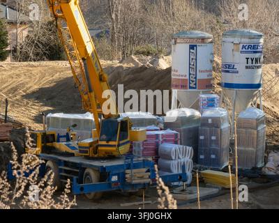Szklarska Poręba, Polen – 18. Dezember 2025: Kreisel-Silos stehen neben einem gelben Mobilkran und gestapelten Isolationsmaterialien auf einem Baugrundstück für ein Stockfoto