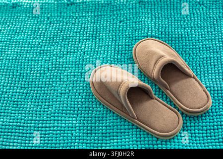 Paar braune beige weiche Wildlederpantoffeln auf heller türkisfarbener Bobbel-Badematte Stockfoto