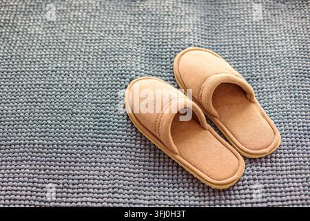 Paar Beige-Tan-Weiche-Samt-Hausschuhe auf grauer Plüsch-Badematte mit Noppen in neutralen Tönen Stockfoto