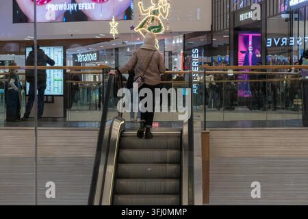 Wroclaw, Polen – 9. Dezember 2025: Einkäufer gehen in der Nähe der Rolltreppenstufen in einem hell erleuchteten Indoor-Handelszentrum, das eine festliche Atmosphäre ausstrahlt Stockfoto