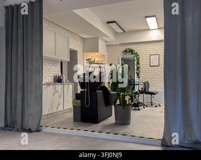 Ein elegantes Friseurstudio-Setup präsentiert eine Waschschüssel, einen Spiegel und minimalistische Möbel und bietet eine helle, zeitgemäße Umgebung für expertisches Stylen Stockfoto