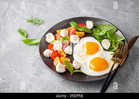 Spiegeleier und Caprese-Salat mit Tomaten, Mozzarella und Basilikumblättern auf einem Teller. Stockfoto