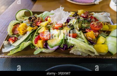 frischer Avocado- und Mangosalat mit Salat, Gurke, Tomaten und Samen, serviert auf einem Teller als gesundes Gourmetgericht. Stockfoto