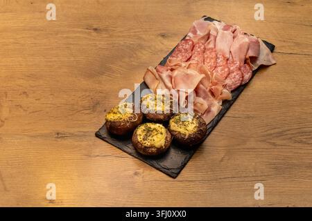 Charcuterie-Platte mit gepökelten Fleischsorten und gefüllten Pilzen, präsentiert Gourmet-Vorspeisen und herzhafte Party-Catering-Gerichte. Stockfoto