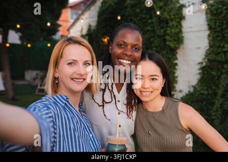 Verschiedene Frauenfreundinnen lächeln und machen ein Selfie auf einer Outdoor-Party Stockfoto