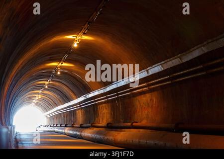 U-Bahn-Tunnel-Innenraum mit gewölbter Betondecke, beleuchteten Lampen und industriellen Rohren, große Nahaufnahme Stockfoto