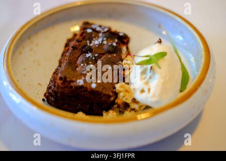 Gourmet-Schokoladenbrownie-Servierstück mit Vanilleeis und essbarer Garnierung in einer Keramikschale Stockfoto