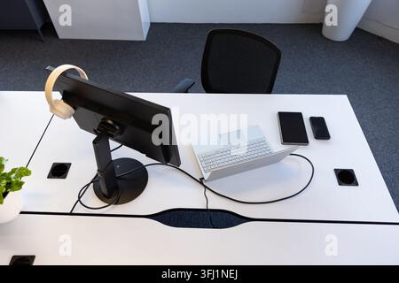 Die Workstation verfügt über einen schwarzen Monitor mit Kopfhörern, einen weißen Laptop und ein Smartphone auf dem Tisch Stockfoto