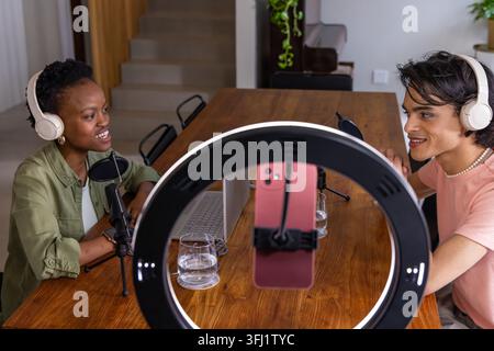 Verschiedene Co-Hosts sitzen zu Hause und nehmen Podcasts mit Ringlicht-Smartphone, Mikrofonen und Laptop auf. Duo, Moderatoren, Interview, Diskussion, Studio, MI Stockfoto
