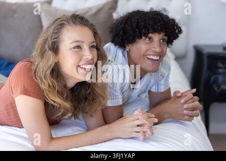 Paare liegen auf dem Bett mit weißer Bettdecke und Kissen im Schlafzimmer, lächeln und beobachten aus der Kamera. Partner, Liegen, Matratze, Bettwäsche, Sonnenlicht, gemütlich, Rela Stockfoto