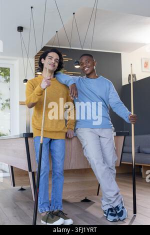 Verschiedene Jugendliche männliche Freunde lehnten sich auf den Billardtisch und posierten in der modernen Spielelounge mit Billardzeichen. Jugend, Duo, Billard, Gesellschaft, zeitgenössisch Stockfoto