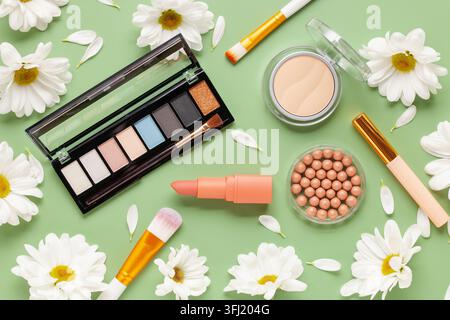 Dekorative Kosmetik und weiße Chrysanthemen auf grünem Hintergrund. Draufsicht. Flache Lagen Stockfoto