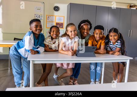 Verschiedene Klassenkameraden im Schulalter, die sich beugen und das Tablet auf Folio am Klassentisch beobachten. Schüler, Zusammenarbeit, Lernen, Gerät, Bildschirm, scho Stockfoto