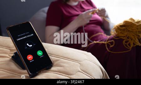 Eine Frau strickt neben einem Smartphone, das einen eingehenden Anruf anzeigt, und veranschaulicht ein Anti-Scroll-Hobby und persönliche Zeit, die fern vom Bildschirm verbracht wird. Stockfoto