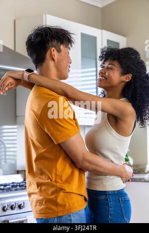 Diverse Paare, die sich umarmen und lächeln, während sie in einer modernen Küche mit Edelstahl-Sortiment stehen. Romantik, Umarmung, Partner, Zweisamkeit, gemütlich, Wärme Stockfoto