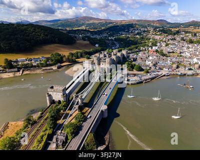 Hohe Blickwinkelansicht einer historischen ummauerten Stadt mit mittelalterlicher Burg, Hängebrücke und Eisenbahnbrücke, die die Mündung an einem sonnigen Tag überspannen Stockfoto