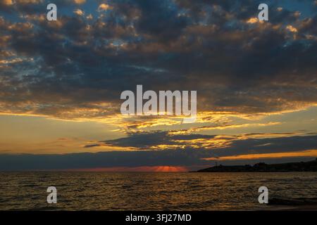 Ruhiger goldener Sonnenuntergang über dem Meer mit weichen Wolken am Horizont Stockfoto