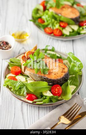 Frischer Gemüsesalat und gebackener Lachs auf einem Teller auf dem Tisch. Mediterranes Ernährungskonzept Stockfoto