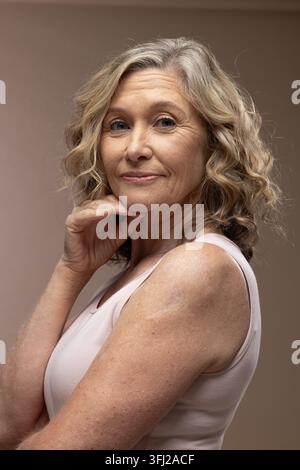 Seniorin stützt das Kinn mit der Hand, posiert im Studio mit hellrosa ärmellosem Oberteil und Halskette Stockfoto