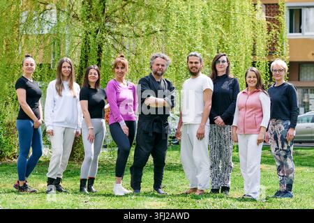 Eine vielfältige Gruppe von Erwachsenen und zwei Instruktoren stehen nach einer Outdoor-Wellness- und Fitnesseinheit zusammen in einem Stadtpark und vermitteln Gemeinschaft und Gesundheit Stockfoto