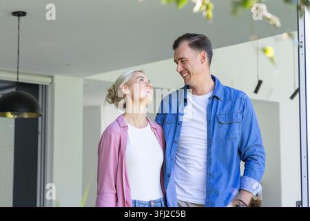 Paar steht sich in der Haustür gegenüber, Frau schaut nach oben, Pendelleuchte hängt links. Romantik, Interieur, modern, Haus Stockfoto