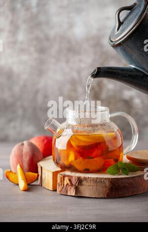 Früchtetee mit Pfirsichen, Minze und Äpfeln in einem Glaskessel auf dem Tisch. Stockfoto