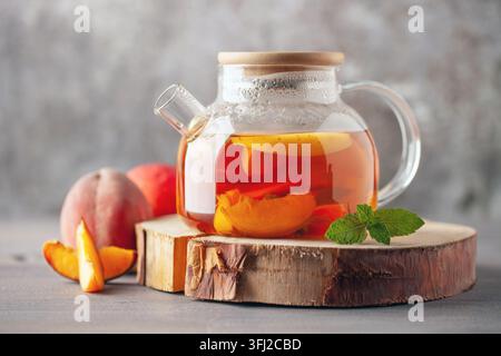 Früchtetee mit Pfirsichen, Minze und Äpfeln in einem Glaskessel auf dem Tisch. Stockfoto