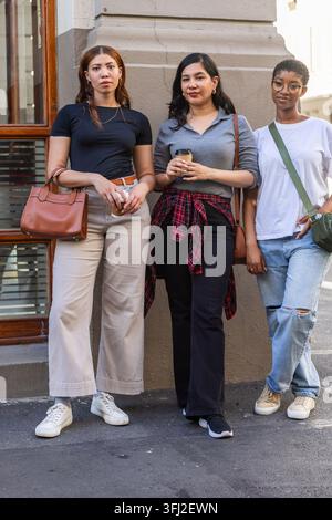 Das weibliche Trio steht an der Stucksäule und einem Holzfenster auf dem Bürgersteig mit Kaffee, Taschen und Turnschuhen. Urban, Streetstyle, lässig, Freundschaft, Gruppe, Tag Stockfoto