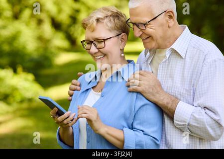 Seniorenpaar lacht, während es im Park mit dem Smartphone lernt Technologie im Freien Stockfoto
