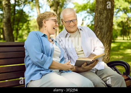 Lächelnde Senioren lesen gemeinsam ein Buch auf einer Parkbank und genießen die Entspannung Stockfoto