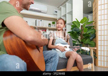 Vater und Tochter spielen zu Hause Gitarre und Ukulele auf dem Sofa Stockfoto